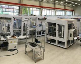 Foto der Montageanlage der Firma Gluth, viele Maschinen sind zu sehen und ein Roboterarm, drei Mitarbeiter arbeiten