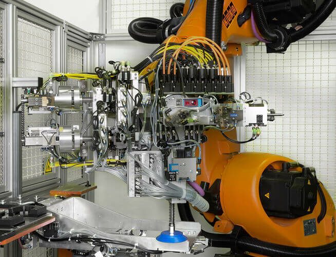 Potideckelmontage, orangener Roboterarm mit bunten Kabeln