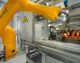 Laserheften, Maschine von innen, gelber Roboterarm in der Mitte bewegt sich und fügt etwas seitlich in die Maschine ein