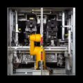 Prüfstand für Druckbegrenzungsventil auf schwarzem Hintergrund, gelber Roboterarm