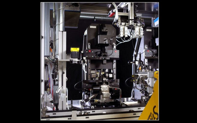 Prüfstand für Druckbegrenzungsventil auf schwarzem Hintergrund, gelber Roboterarm