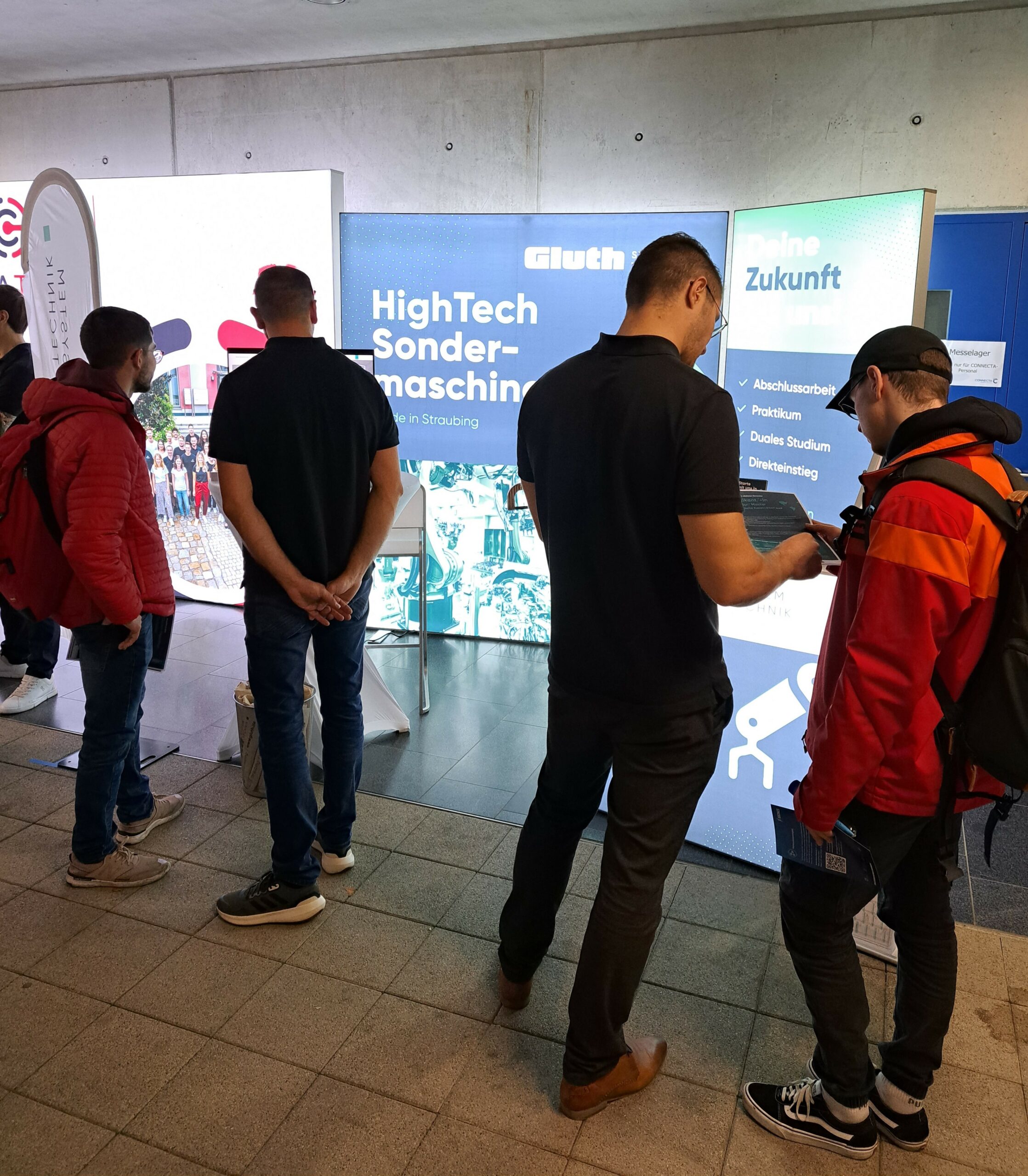 Connecta Messe 2023, vier Männer stehen vor dem Stand, zwei in schwarzen T-Shirts, zwei in roten Jacken